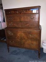 Front view of the tall wooden dresser showing burled wood veneer, floral carving, brass handles, and overall condition.
