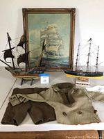 Wide shot showing full lot on white table: two tall ship models, framed ship print, and child’s sailor outfit (jacket and shorts).