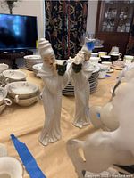 Photo showing two ceramic Asian figurines with green accents on a beige tablecloth with dishes in background
