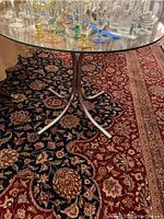 Full view of the round beveled glass top table on a decorative rug with various glassware on the table top.