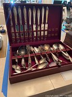 Photo of an open wooden box containing mostly matching knives, forks, spoons, and serving utensils, some tarnished, on velvet lining.