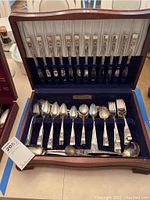 Photo of full flatware set arranged in wooden storage box with blue velvet interior, showing silver plate pieces and floral pattern on handles.