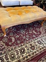 Full view of the mustard yellow tufted velvet bench with wooden legs on a patterned carpet