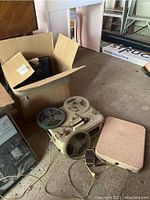 Overall view of vintage Sony tape recorder with wires and case nearby, box in background contains record sets.