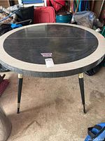 Front view of the round table showing the two-tone wood surface and black legs with brass accents.