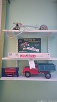 Shelf with desk lamp on top, Trump Plaza Texas Hold 'Em poker set and Monopoly game boxes in middle, Tonka dump truck and Corgi double decker bus box at bottom.