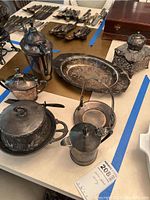 Overview of 7 silverplated serving pieces including trays, kettles, teapots, and ornate lidded container showing tarnish and wear.