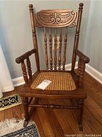 Front view of vintage child-sized rocking chair showing carved backrest and cane seat.