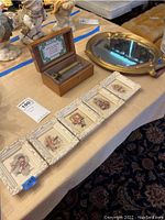 Wide view of the music box in wooden box alongside the five small framed children's instrument prints and a gold tray.