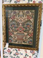 Full view of the framed needlepoint tapestry showing floral arrangement in a basket bordered by a green mat and gold decorative frame.