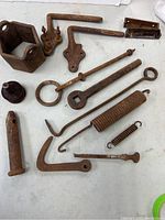 Top-down view of lot showing 14 rusted metal pieces including springs, hooks, rings, and latch hardware