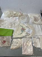 Multiple hand embroidered doilies and dresser scarfs displayed together including a green fabric piece and floral embroidered pieces.