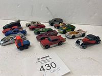 Overview photo showing 15 assorted vintage toy cars and vehicles in various colors and styles arranged on a flat surface.