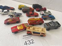 Overview photo showing 15 vintage metal die cast toy vehicles of various types and colors arranged in rows on a white surface.