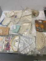 Lot showing an assortment of embroidered doilies, handkerchiefs, and chair arm covers in various shapes and embroidery styles, mostly in white and cream tones.
