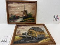 Two framed folk art oil paintings showing Dutch scenes with mills, displayed together.