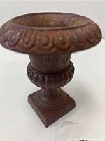 Front angle view of the small antique cast iron urn showing the embossed decorative rim and weathered surface.