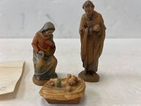 Full view of the three hand carved religious figurines including Mary seated, Joseph standing, and baby Jesus lying in a manger.