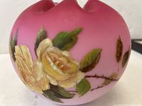 Close-up view of yellow handpainted roses with green leaves and thorny stems on cranberry glass bowl surface.