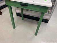 Wood table with green painted legs and base, white enamel graniteware top with drawer and black handle