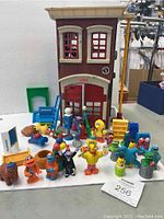 Front view of Fisher Price Sesame Street brownstone playset with assorted Sesame Street character figures and accessories arranged on white surface.