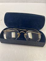 Closed hard blue case open to display antique gold wire glasses inside.