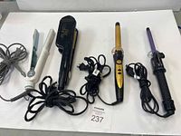 Full view of four hair styling tools on white surface including two flat irons and two curling devices with power cords.