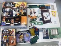 Lego Hello Neighbor boxes and loose pieces. One box for Neighbor's House set, second smaller box for Basement Door set. Lego bricks and parts including walls, windows, door pieces, green baseplate, and three character figurines laid out on surface.