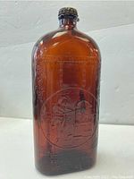 Front view of amber glass bottle with embossed blacksmith working at anvil scene.