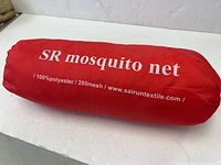 Red cylindrical bag with white print stating 'SR mosquito net 100% polyester 280mesh'