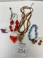 Full view of lot showing red-white pendant necklace, amber seahorse bead necklace, blue bead bracelet, and two pairs of earrings.