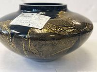 Close-up of black glass vase with gold mica leaf decoration and a label showing the artist's name and price.