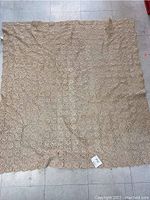 Full view of the vintage crocheted needlework tablecloth laid flat on a tiled floor showing overall size and shape