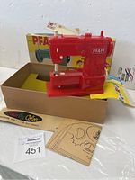 Red Pfaff toy sewing machine on top of the box with fabric and pattern sheets visible.