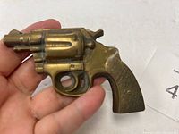 Front view of the solid brass revolver belt buckle held in hand, showing detail of the revolver shape and textured grip.