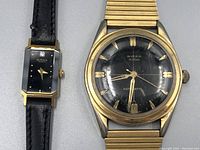 Close-up of men's automatic Birks Rideau watch showing black dial, gold markers, scratches on crystal, and gold expandable bracelet.