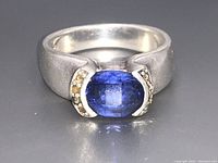 Front view of silver ring focusing on faceted blue oval stone with accent stones on each side.
