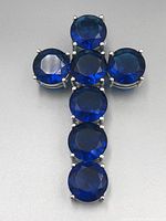 Close-up photo of a cross pendant composed of seven round, faceted deep blue gemstones set in 925 sterling silver with prong settings, showing the front view.