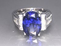 Front view of silver ring with deep blue oval faceted center gemstone and clear stones on shoulders.