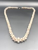 Full view of the coral bead necklace laid flat showing the graduated beads twisted in two strands with black clasp.