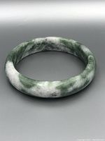 Front view of the jade bangle showing the mix of green, white, and dark mottled colors with a smooth polished finish.