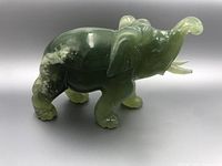 Side view of the green jade elephant figurine showing polished surface, carved ears, trunk, legs, and tail with natural veining in the stone.