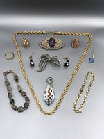 Jewelry lot laid out with all pieces visible on a black background including necklaces, bracelets, earrings, rings, brooches, and pendants.