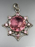 Close-up photo of the front of the vintage pink gemstone pendant showing the large central round pink stone with six smaller surrounding pink stones set in a silver filigree frame.