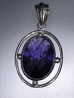 Front view of purple faceted oval gemstone pendant set in sterling silver oval with three silver ball accents and decorative bail.