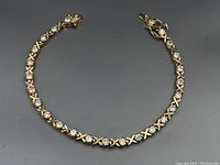 Full view of silver tennis bracelet showing the complete circle of alternating round clear stones and silver X-shaped links with clasp visible.