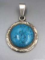 Straight-on view of round sterling silver pendant with deep blue turquoise cabochon stone with matrix patterns in center.