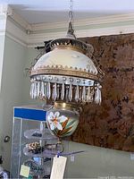 Full view of the chandelier hanging, showing metal frame, painted floral glass, and hanging prisms.