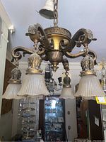 Full view of the chandelier showing six textured glass shades and ornate brass finish metal arms with decorative scrollwork and floral details.