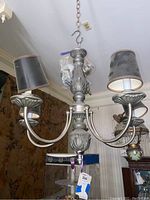 Photo showing metal chandelier with four tall black tapered shades on lights, one shade missing.